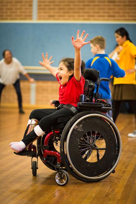 Girl in wheel chair, smiling with hands in the air