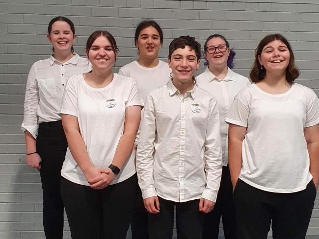 group of students standing together in white shirts and black pants