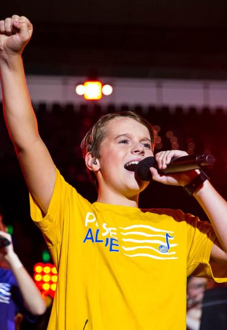 A student wearing a yellow Pulse Alive t-shirt singing, with one fist raised up