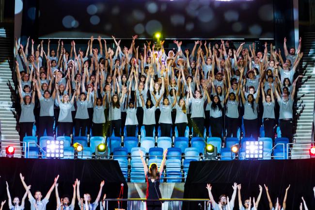 Student choir in a stadium holding their hands above their heads