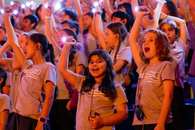 A choir singing, wearing Pulse Alive t-shirts and holding a lit flashlight over their heads