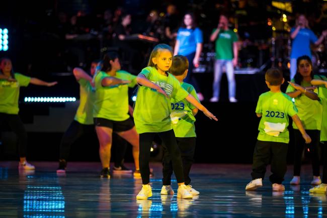 An ensemble of dancers wearing green Pulse Alive t-shirts, standing with one arm out and the other arm bent in front of them