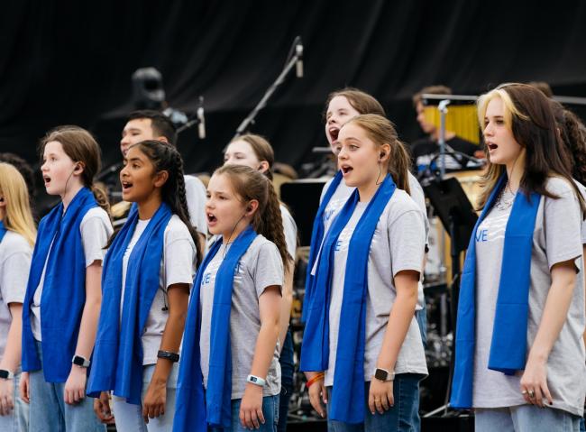 A choir wearing grey Pulse Alive t-shirts and blue scarves