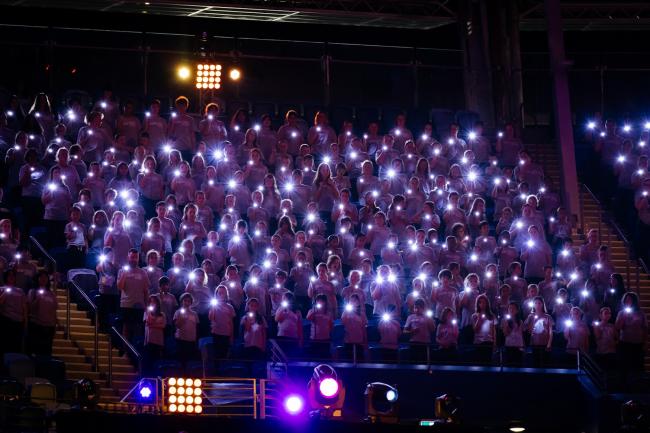A choir in a stadium holding lit flashlights