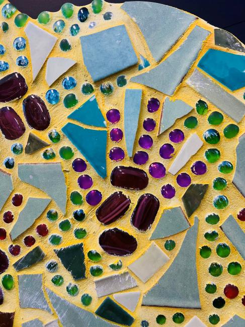 A close-up of one of the handprints from the mosaic artwork ‘Our Individuality Creates Beauty’. The palm is made from deep red and purple stones, and the fingers from translucent purple stones.