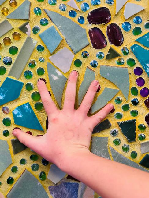 A close-up of a student’s hand covering one of the handprints from the mosaic artwork ‘Our Individuality Creates Beauty’.