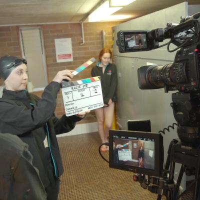 Student wearing a swimming cap holding a clapperboard in front of a camera
