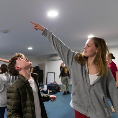 Two students do a warm up in a drama workshop with other students in the background.