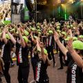 Large group of young people wearing lime green caps and black 'FabuloUS' t-shirts and pants, with their arms in the year. They are standing in front of a concert stage for SpecFest 2023