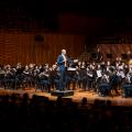 A conductor on stage directing a student orchestra.